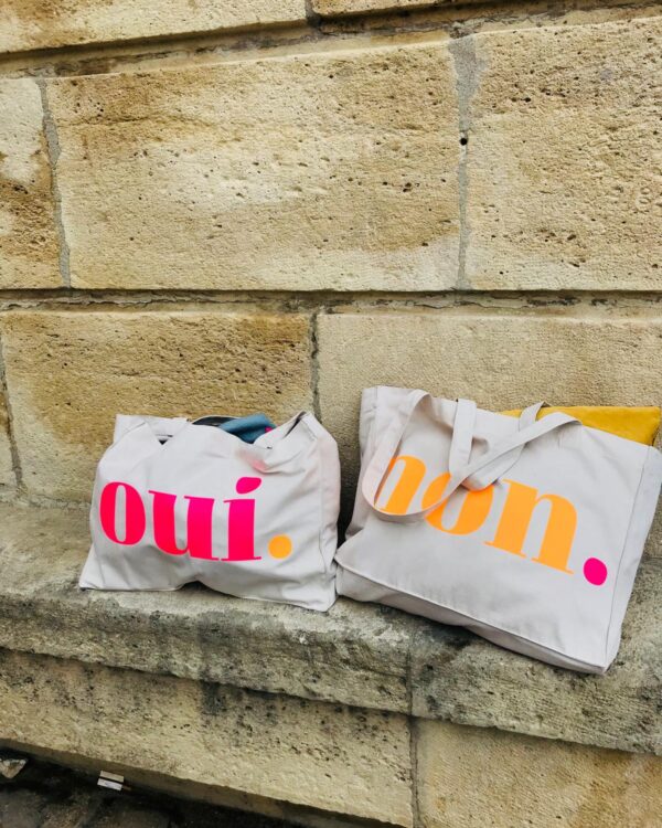 Oui. Non. Shopping Bags in Natural Raw mit Neon-Print vor einer Steinmauer